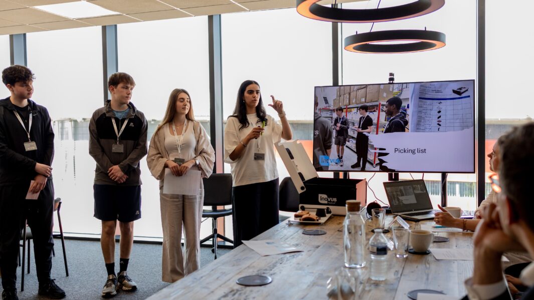 Male and female students stood in boardroom giving a presentation to a panel of judges
