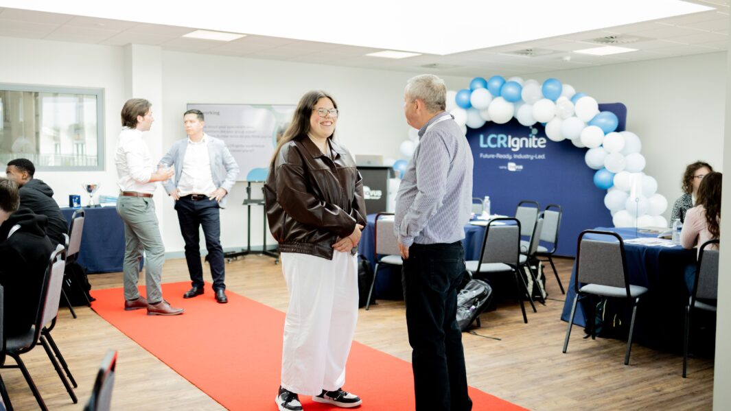 Female student stood up on a red carpet talking to a male mentor