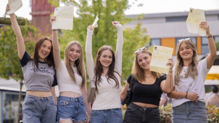 five students holding their results up smiling at the camera
