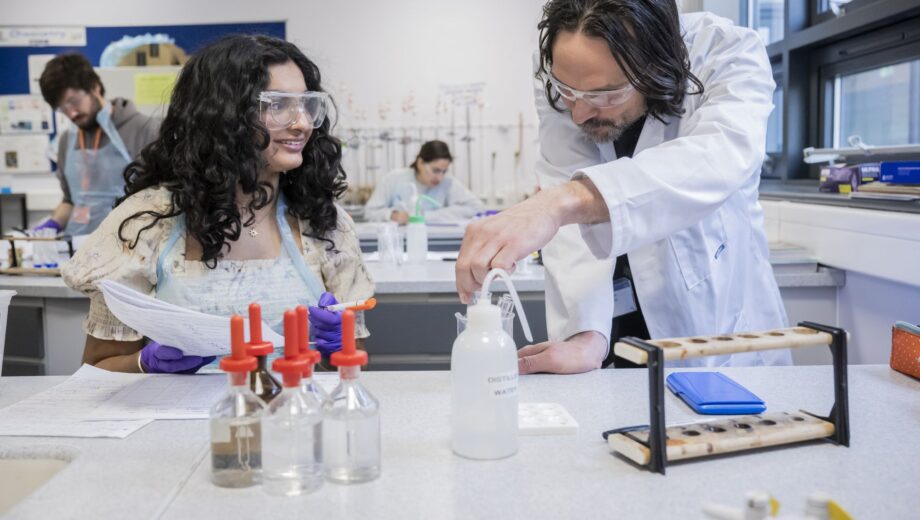 A female student and a male teacher working in a lab wearing lab coats