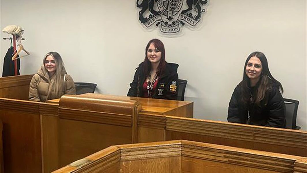 Three female Carmel students sit in courtroom simulation at Edge Hill University.