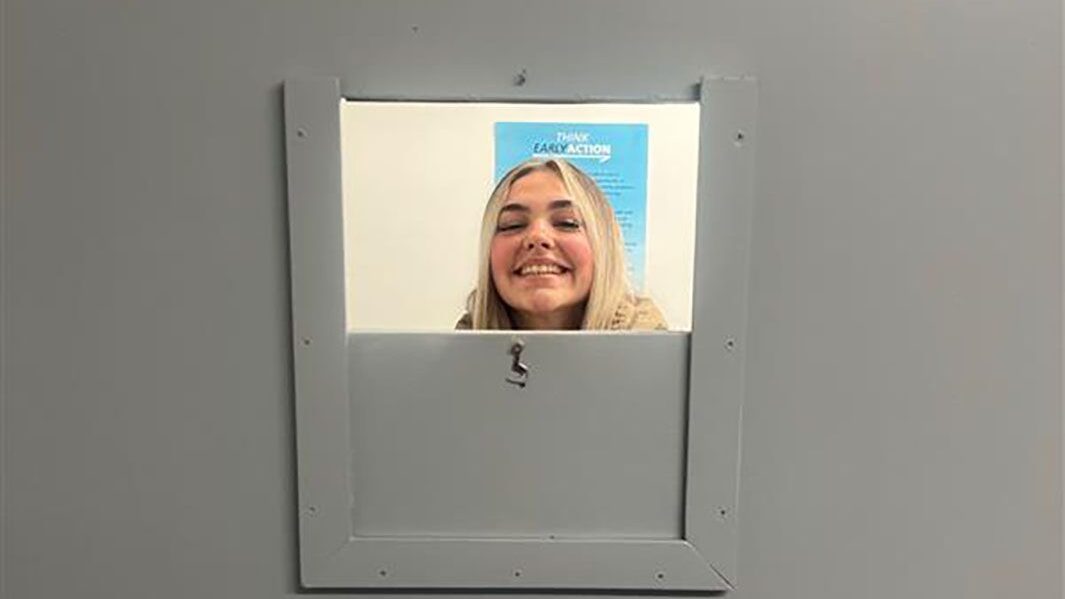Blonde haired female Carmel student smiles through window of holding cell at Edge Hill university's 'Act like a cop' experience.