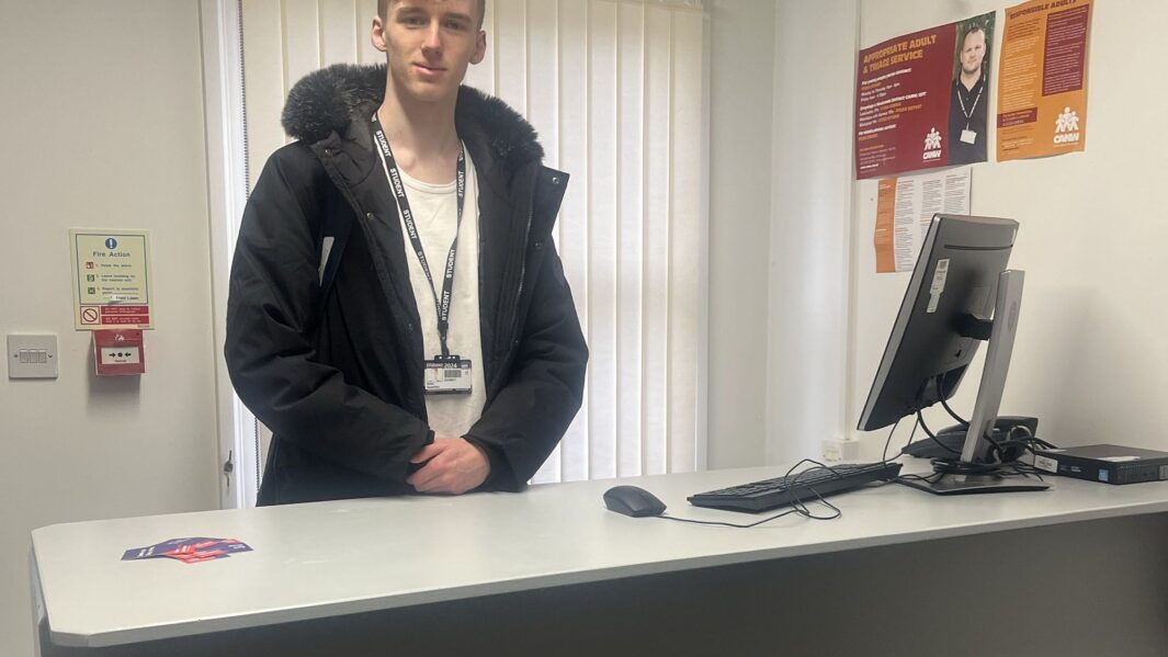 Male Carmel student stand behind processing desk at Edge Hill University's police experience.