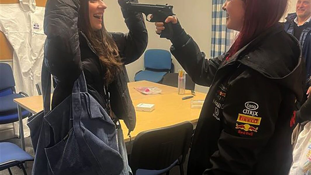 Red haired female student holds brunette haired student at fake gun point in criminal investigation experience at Edge Hill university.
