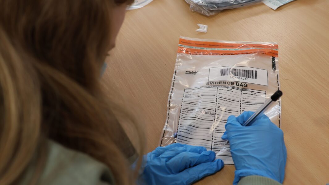 gloved hands of students working in the Criminology classroom looking at evidence