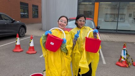 Two students wearing yellow macs washing cars with a red bucket