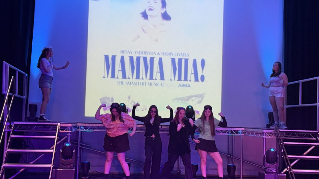Girls singing and dancing on stage in front of a Mamma mia backdrop