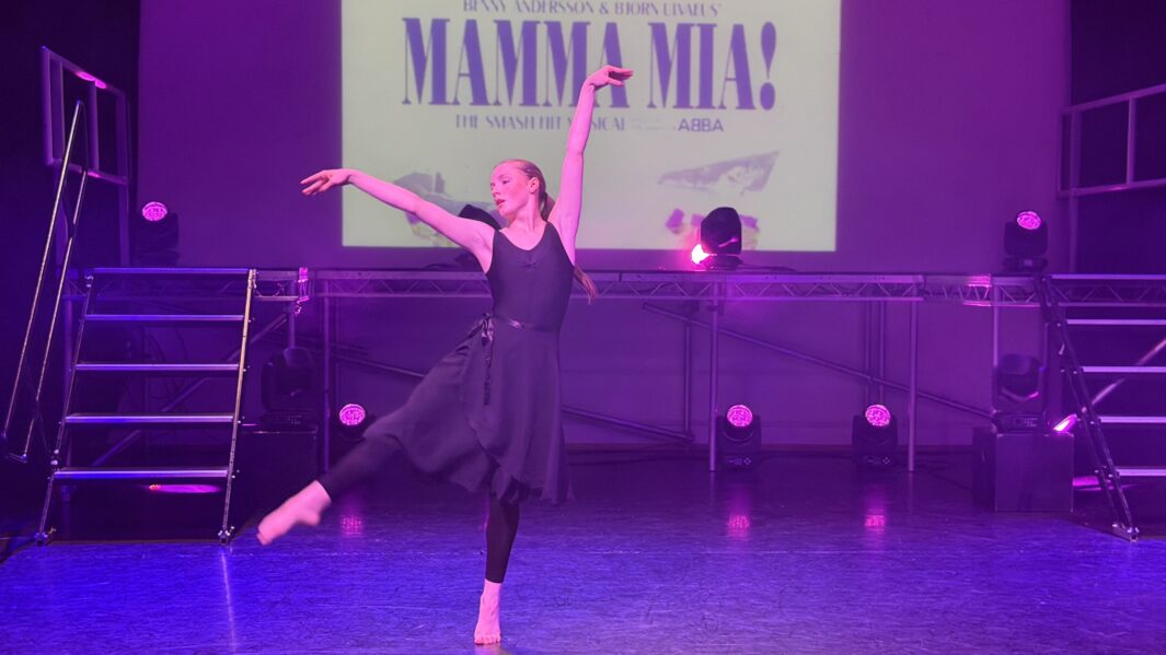 Girl in a black dance outfit doing ballet ion stage in front of a Mamma mia backdrop