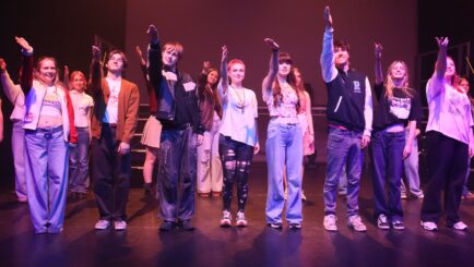 Group of students on stage waving in the finale