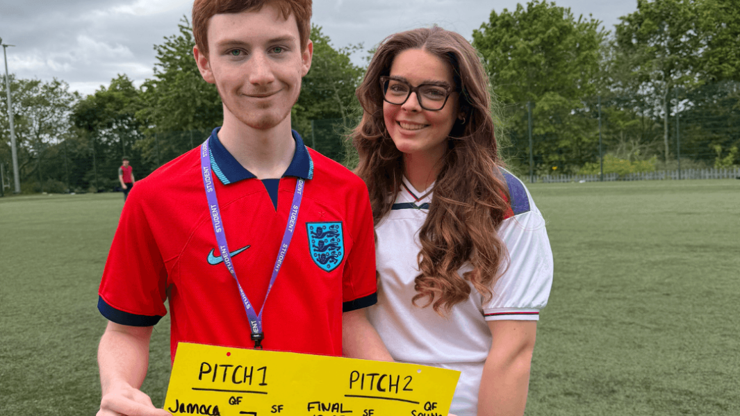 two students holding up poster for charity football event