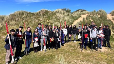 class of 38 students stood in sand dunes on beach
