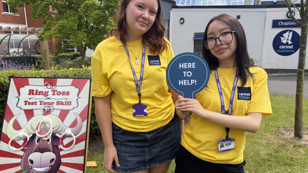 Two girls wearing yellow t shorts holding a happy to help paddle