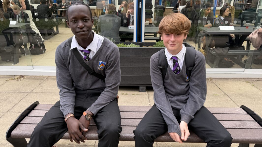 Two boys in grey school uniform sat on a bench