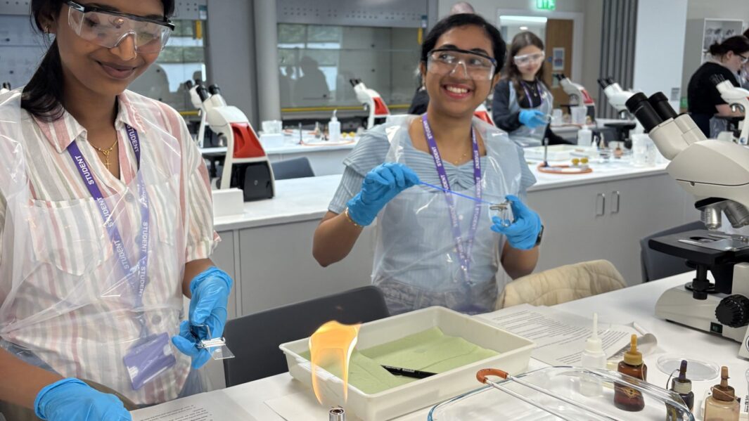 2 female students in a lab wearing plastic aprons and gloves