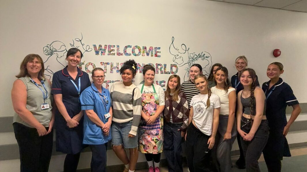 Materinty staff and students stood infront of the mural looking happy